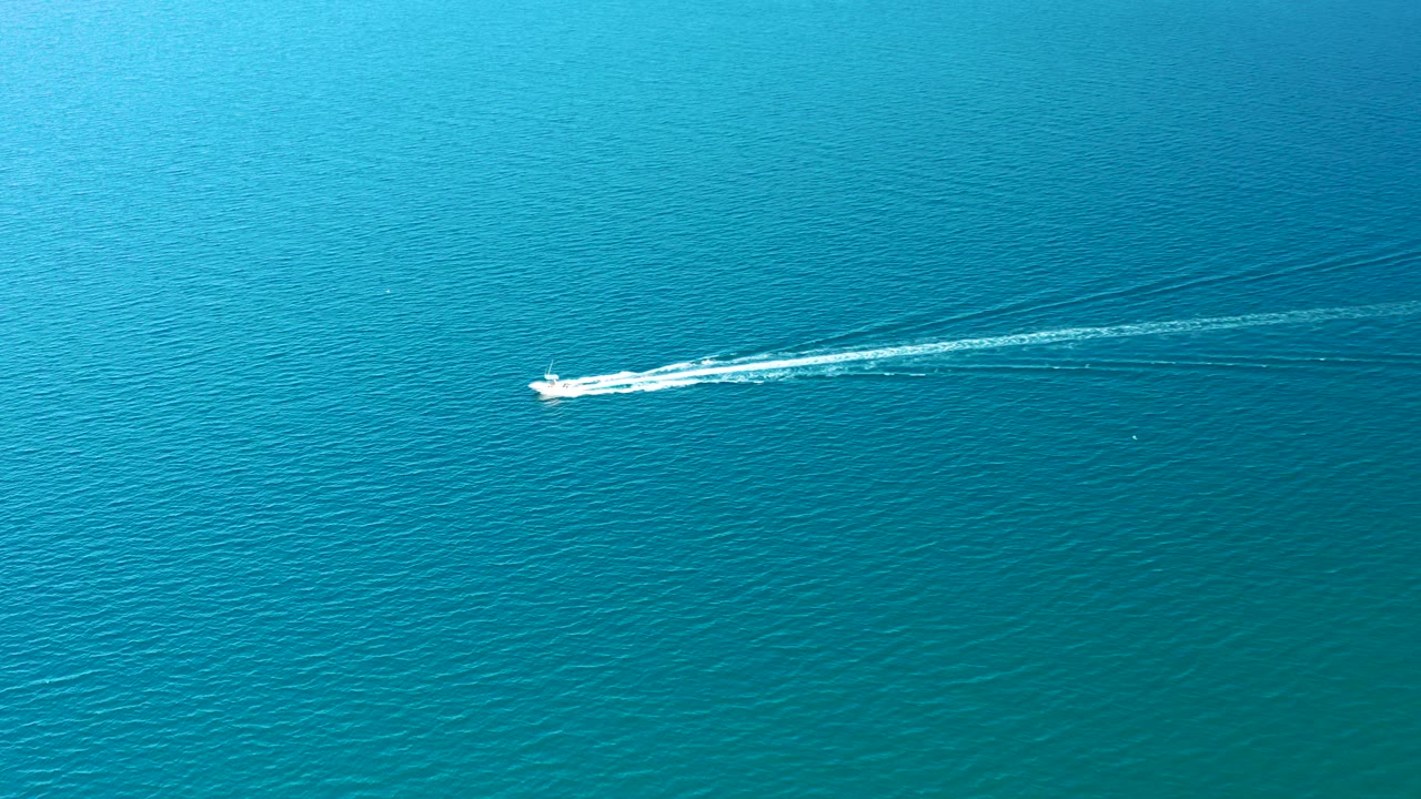 The speedboat crosses open turquoise ocean near Ligui, Baja California Sur, with a curved white wake spreading behind it and no visible people.