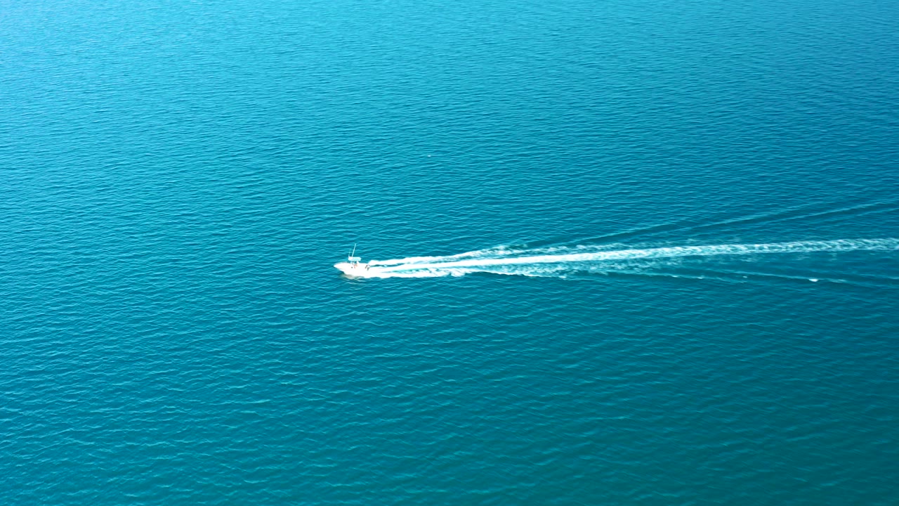 Small white speedboat crossing blue ocean with a trailing white wake.