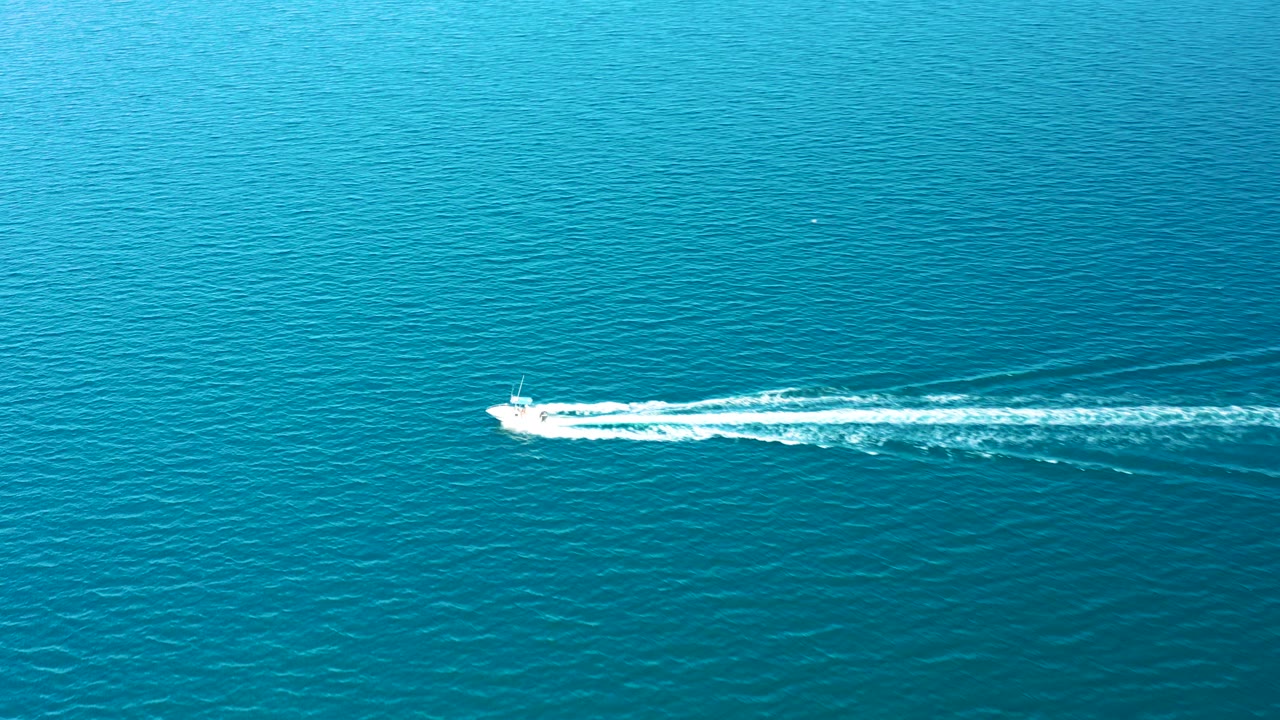 At 0:03 in Ligui, Baja California Sur, the speedboat appears lower in the aerial view, pulling a bright white wake over rippled blue water with no visible people.