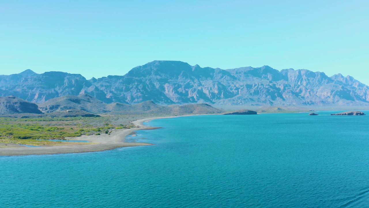 Wide Ligui coastal view with the sandy beach shifted farther left, turquoise bay water across the foreground, small boats near the far shore, mountains across the horizon, and no visible people.