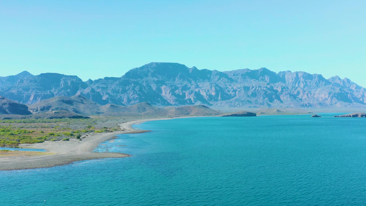 At 0:01, the Ligui coast remains centered with rippled turquoise water below, a pale beach line at left, low coastal vegetation, and distant mountains, no visible people.