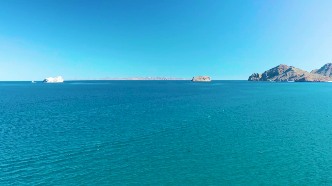 Opening frame over turquoise water near Ligui, Baja California Sur, with a white cruise ship left of center, rocky islands on the horizon, clear blue sky, and no visible people.