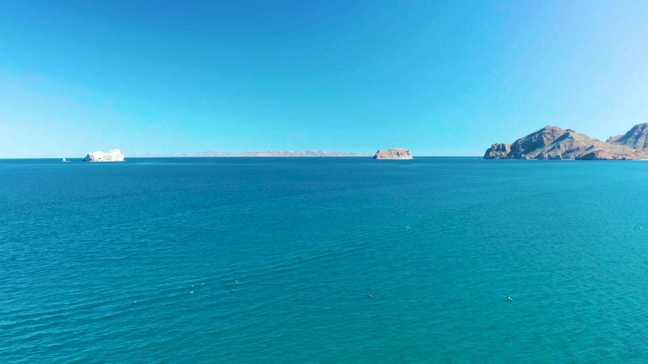 Aerial-looking view of calm turquoise water near Ligui, Baja California Sur, with the white cruise ship slightly farther across the horizon, rocky islands behind it, and no visible people.