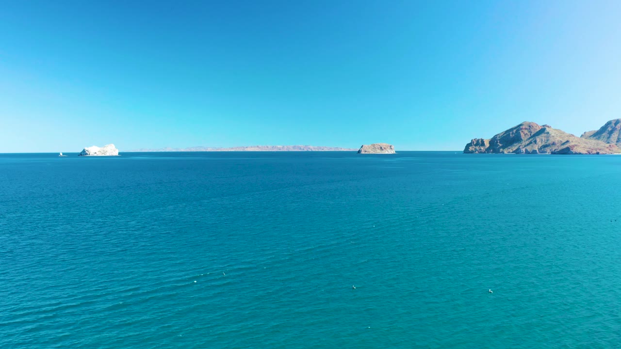 Cruise ship and rocky islands under clear blue sky over turquoise water.