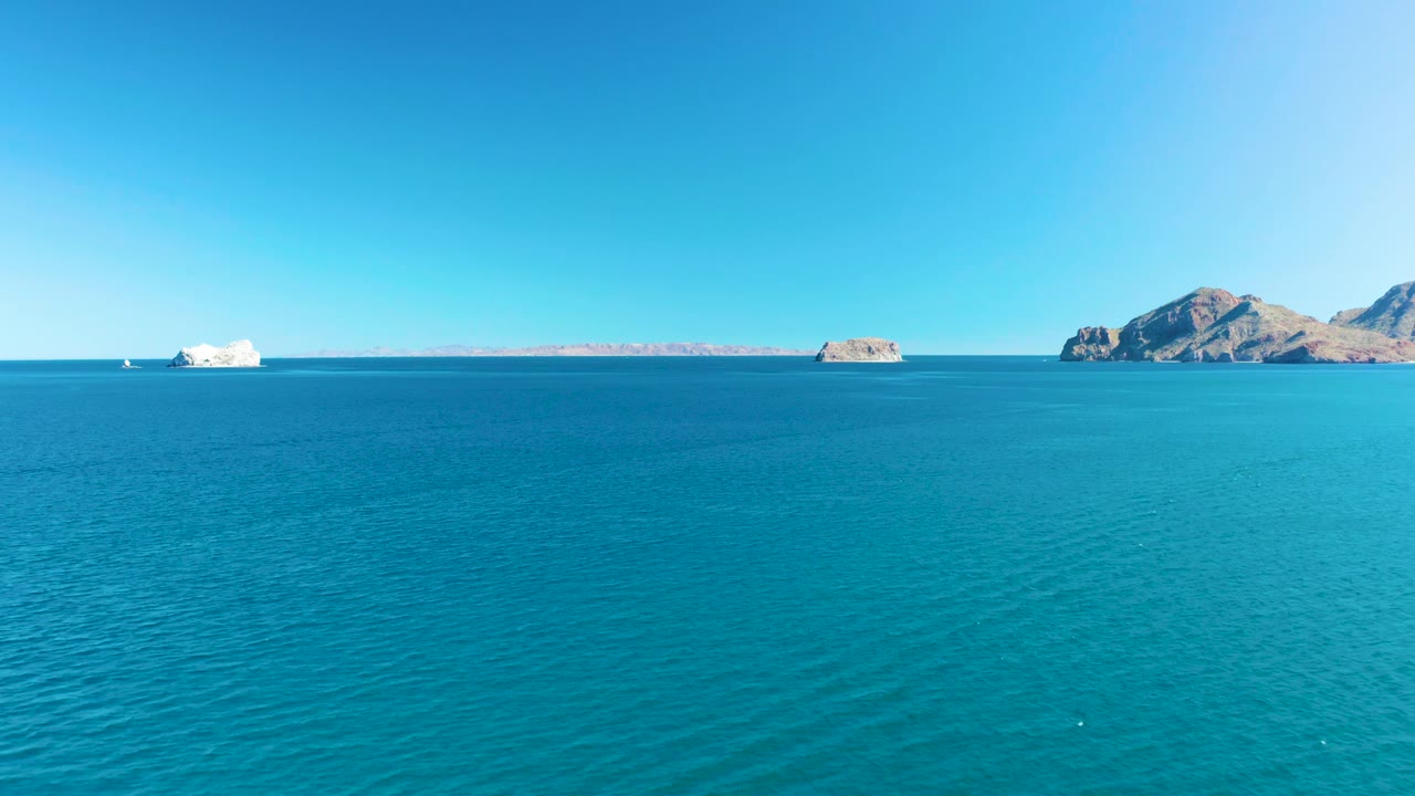 Midway through the clip, turquoise water fills most of the frame, with the Ligui rocky islands and distant land set low against a clear, cloudless sky and no visible people.