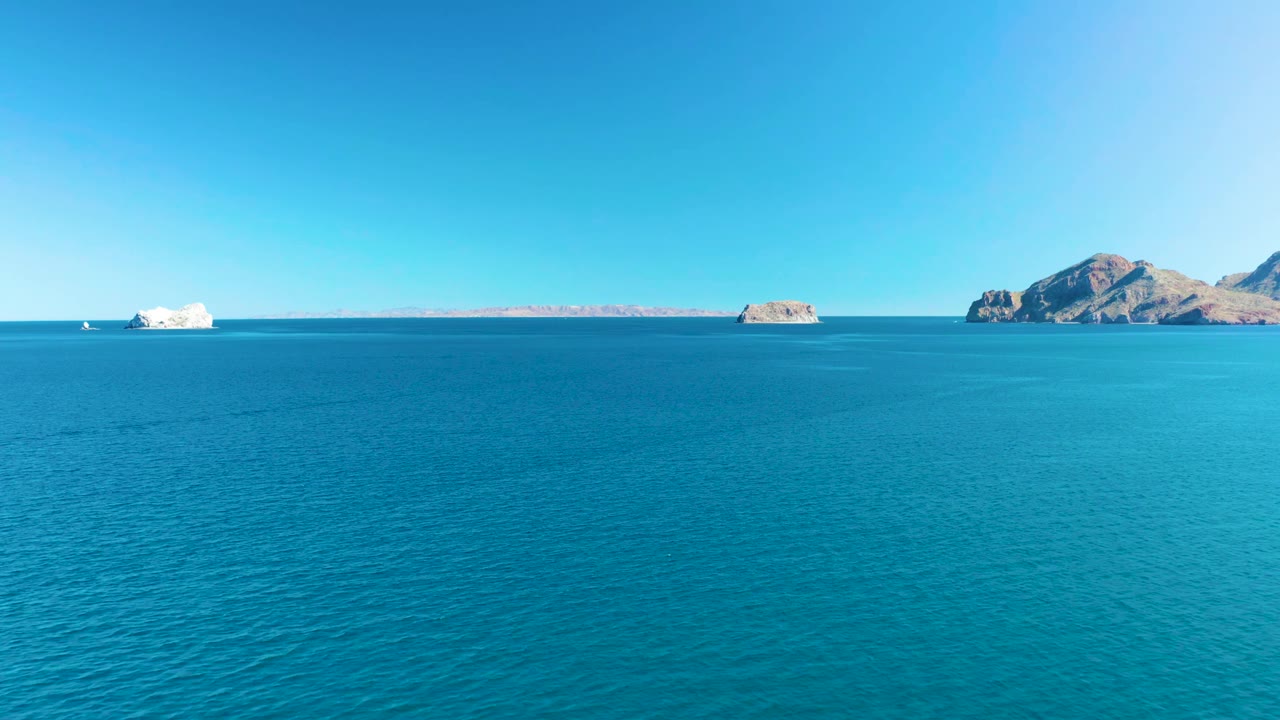 Turquoise ocean stretches toward the horizon in Ligui, Baja California Sur, with the white boat slightly left of the rocky islands and no visible people.