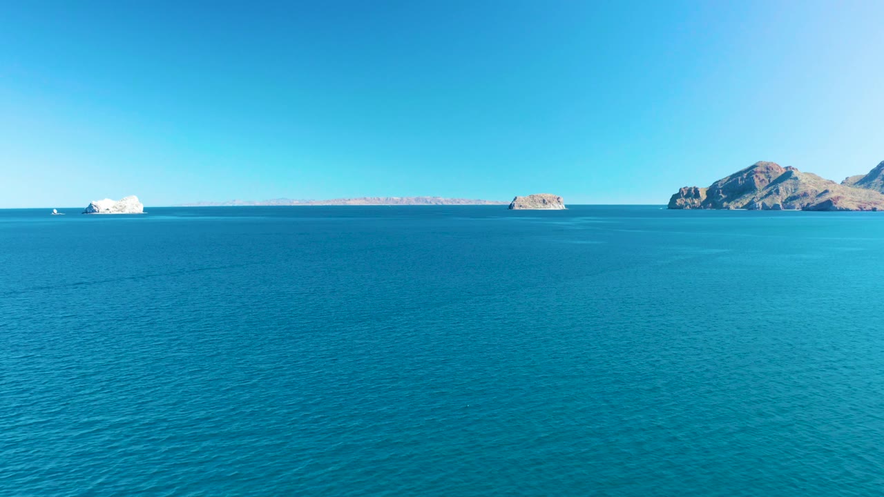 Open turquoise water fills most of the frame in Ligui, Baja California Sur, with a small white boat near the left horizon, low rocky islands, and no visible people.