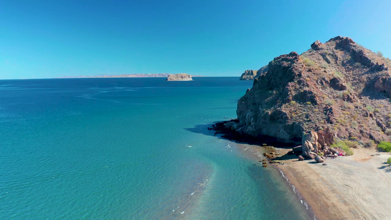 Turquoise ocean curves around a rocky headland beside a sandy beach.