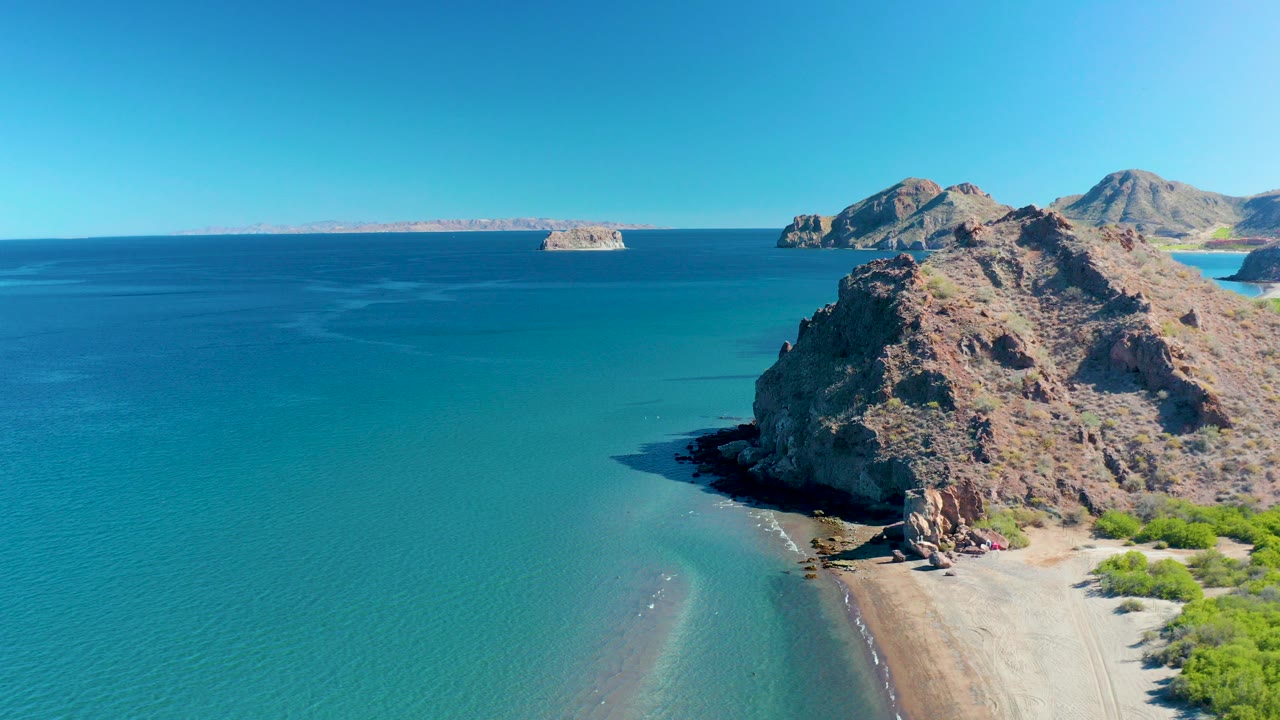 Aerial view of turquoise water beside a rocky coast and sandy beach.