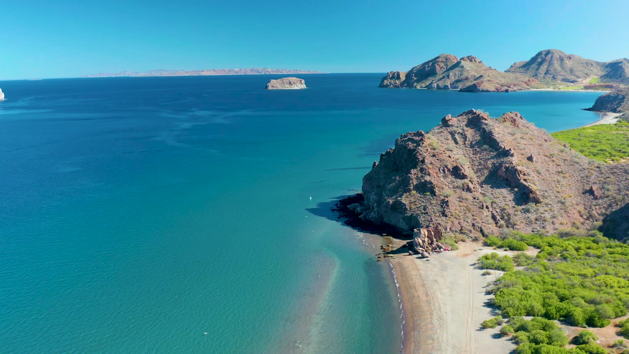 At 0:03 the Ligui shoreline fills the lower right with green brush and sand, while the rocky headland projects into clear turquoise water and no visible people appear.