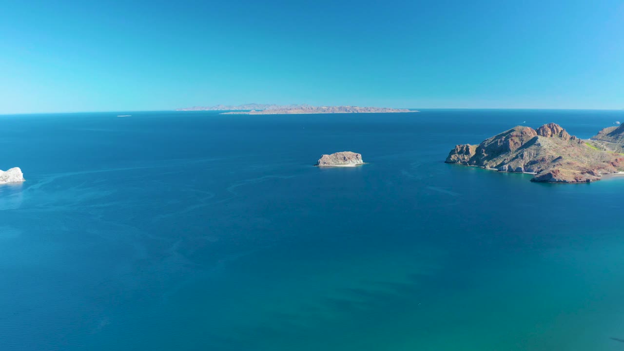 Open blue ocean beneath a clear sky with rocky islands and a distant landmass.