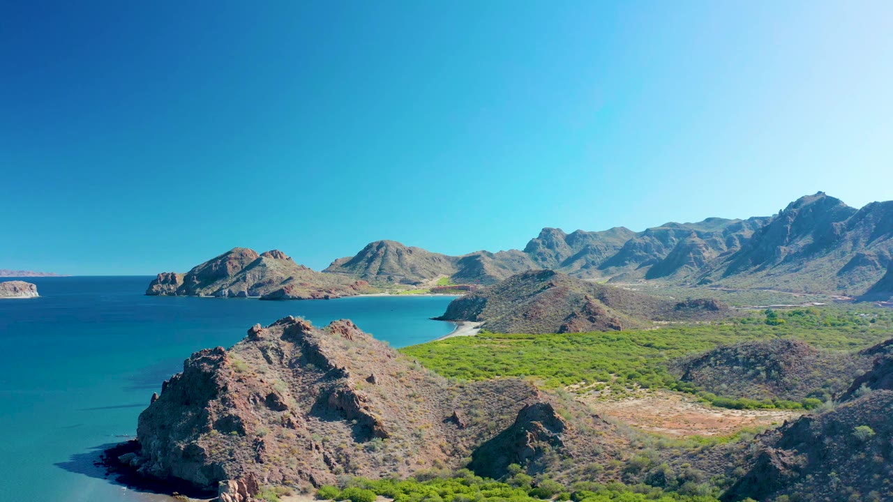 Rocky coastal headland beside turquoise water with beach and mountains behind