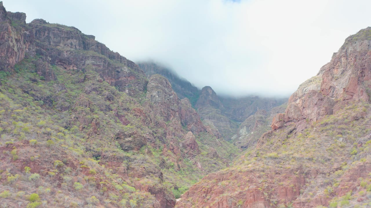 Puerto Escondido mountain ridges fill the frame as white mist rests along the upper rock faces and the central valley stays visible, with no visible people.