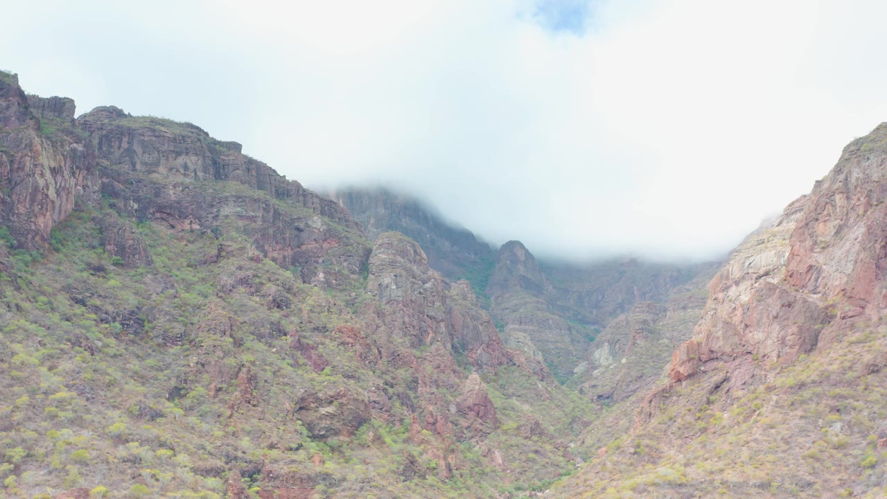 Wide view of a rocky mountain valley in Puerto Escondido, Baja California Sur, with pale cloud covering the upper ridge and no visible people.
