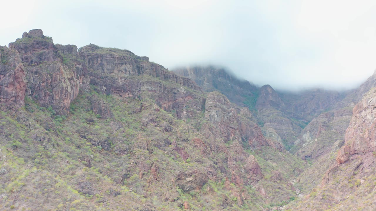 A tall rocky outcrop stands near the center of the Puerto Escondido mountain view as mist softens the higher ridge behind it and no visible people appear.