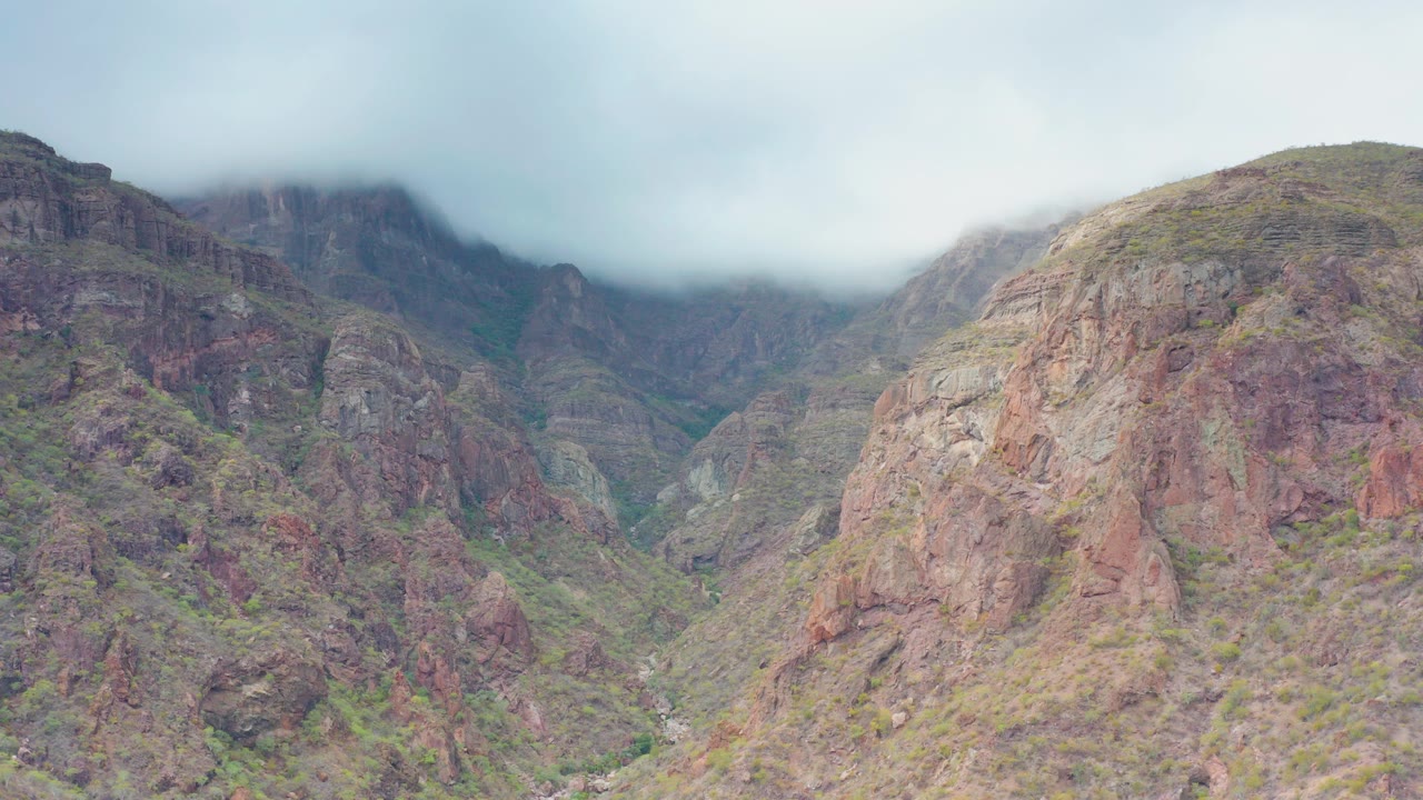 Wide view of a rocky mountain valley in Puerto Escondido, Baja California Sur, Mexico, with low gray cloud covering the upper ridges and no visible people.