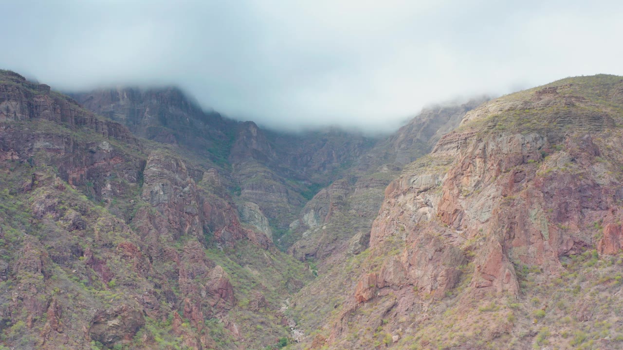 Opening frame of a rocky mountain valley in Puerto Escondido, Baja California Sur, Mexico, with pale cloud cover touching the upper ridges and no visible people.