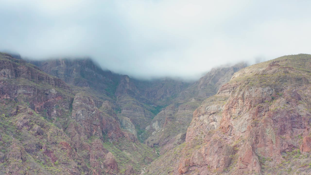 A central rounded ridge in Puerto Escondido, Baja California Sur sits below soft gray cloud cover, with darker canyon walls behind it and no visible people.