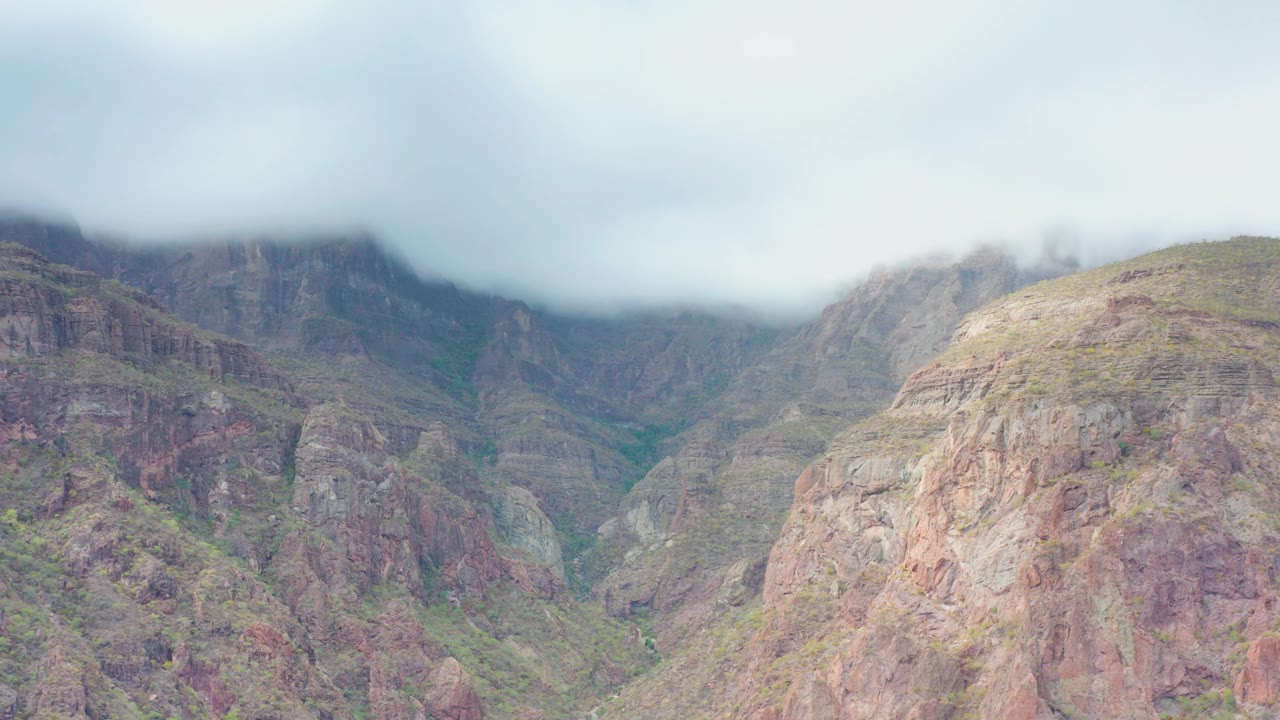 A broad cloud bank sits over rugged cliffs and a central green ravine in Puerto Escondido, Baja California Sur, with no visible people.