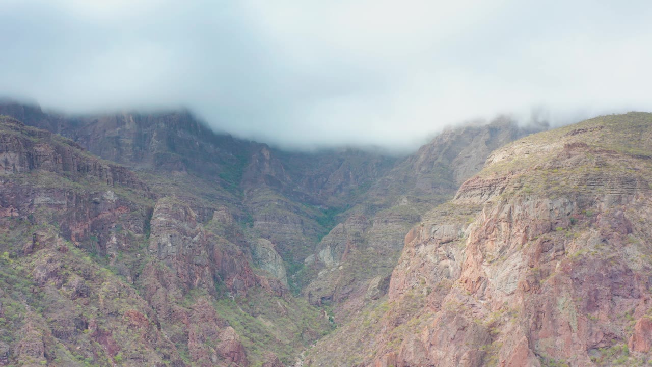 A rounded rocky slope with muted red and tan tones rises beneath low cloud in Puerto Escondido, Baja California Sur, with no visible people.