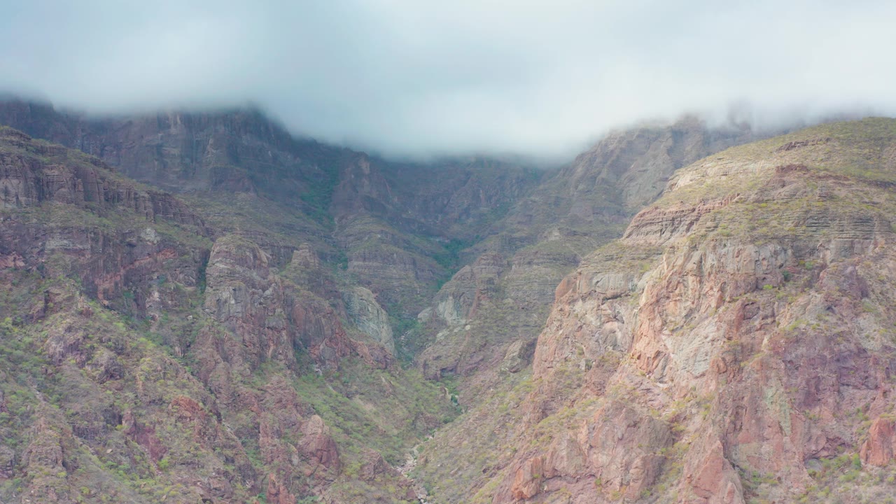 Puerto Escondido, Baja California Sur rocky mountain valley with low clouds over the upper slopes, green gullies, reddish cliff faces, and no visible people.