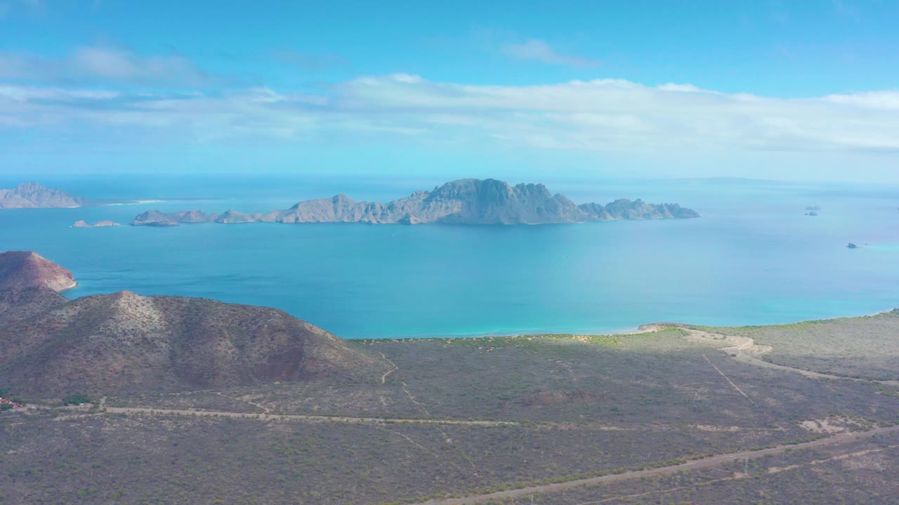 Aerial view of desert coast, blue ocean, offshore islands, and a dirt road.