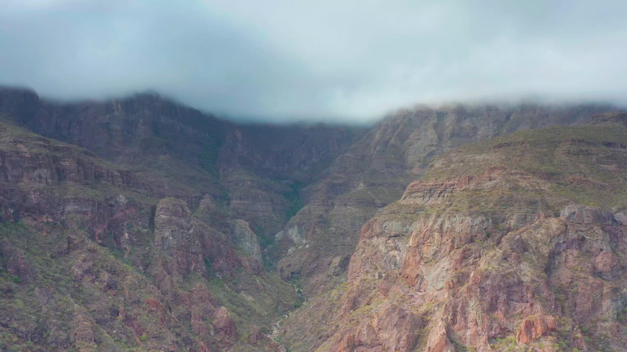 Puerto Escondido mountain ridges remain centered as low clouds press across the upper peaks and the rocky valley stays empty of visible people.