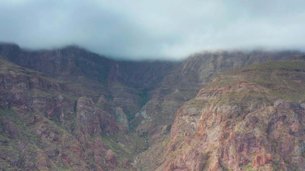 Opening frame of a rocky mountain valley in Puerto Escondido, Baja California Sur, Mexico, with green ravines, muted overcast light, and no visible people.