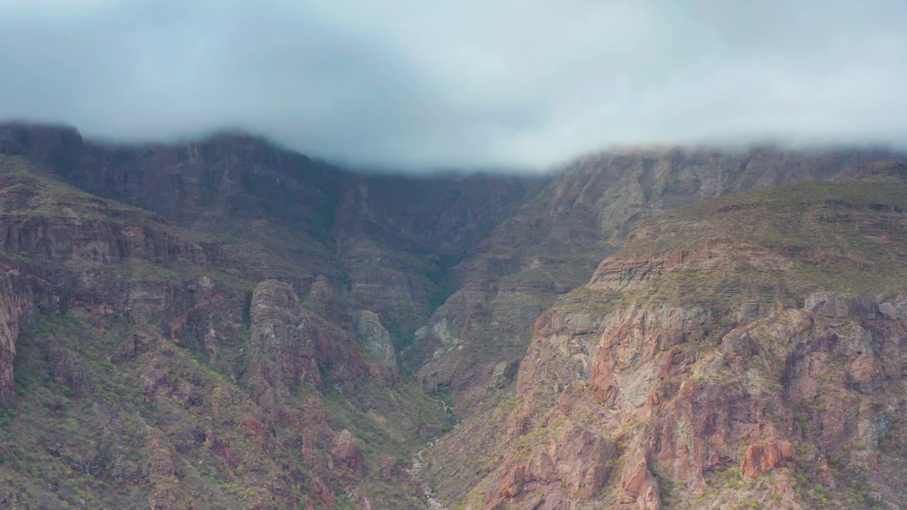 Puerto Escondido, Baja California Sur canyon view with reddish-brown rock faces, green patches in the valley, heavy cloud along the upper ridge, and no visible people.