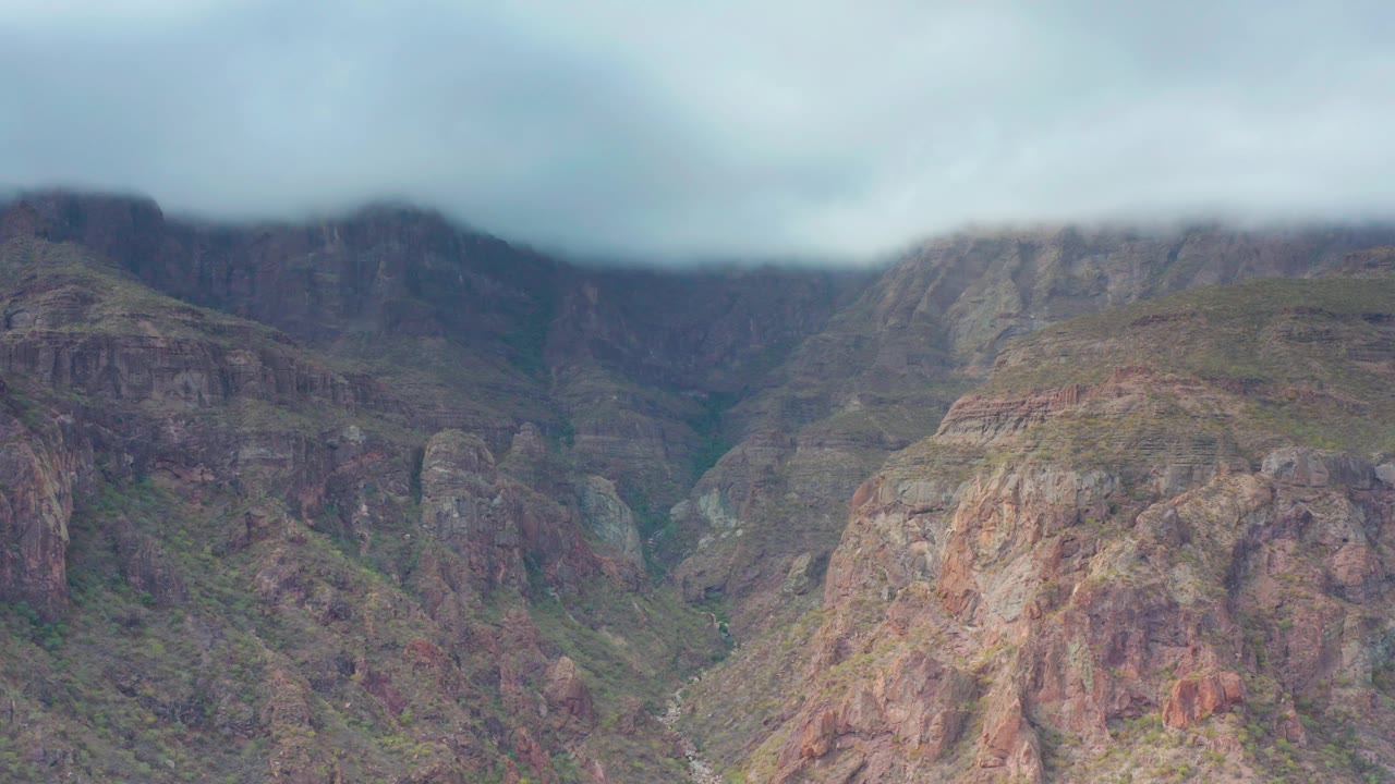 Puerto Escondido, Baja California Sur aerial-style view of rocky cliff bands, a narrow green valley floor, soft overcast light, low clouds, and no visible people.
