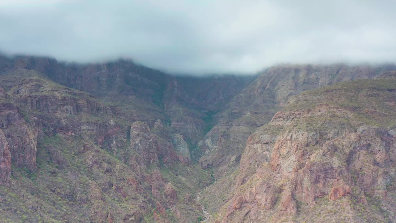 Puerto Escondido, Baja California Sur mountain ridges sit under low pale clouds, with green patches in the rocky valley and no visible people.