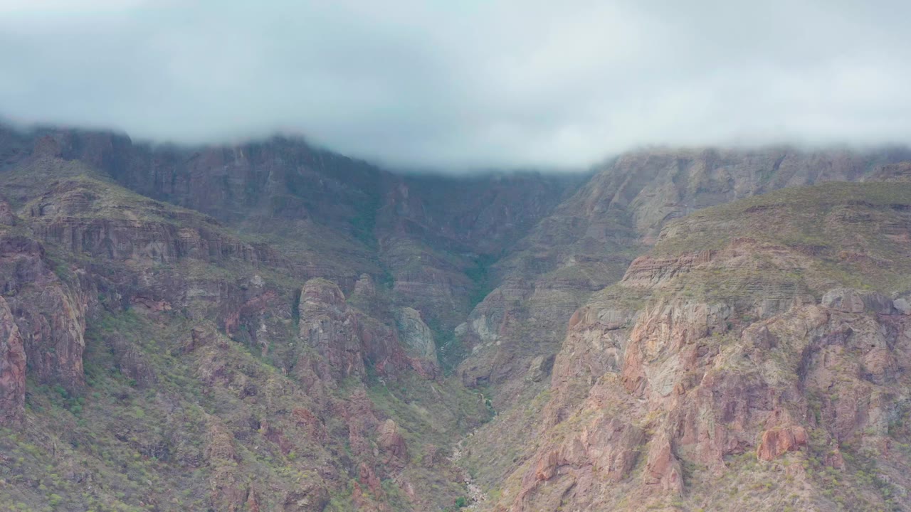 A rocky peak in Puerto Escondido, Baja California Sur fills the center frame while mist-like cloud cover hangs along the upper ridge and no visible people appear.
