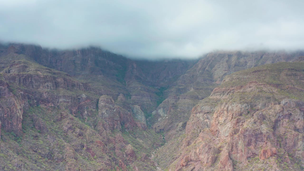Rugged cliffs and dark ravines fill the Puerto Escondido, Baja California Sur view as low cloud cover presses down over the mountain tops, no visible people.