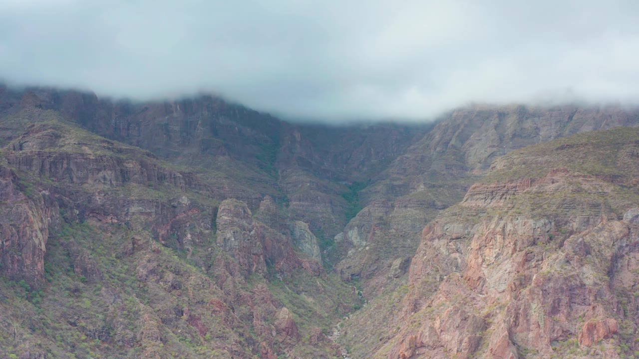 Puerto Escondido, Baja California Sur rugged cliffs under an overcast sky, with muted brown rock, green vegetation in the valley cuts, and no visible people.