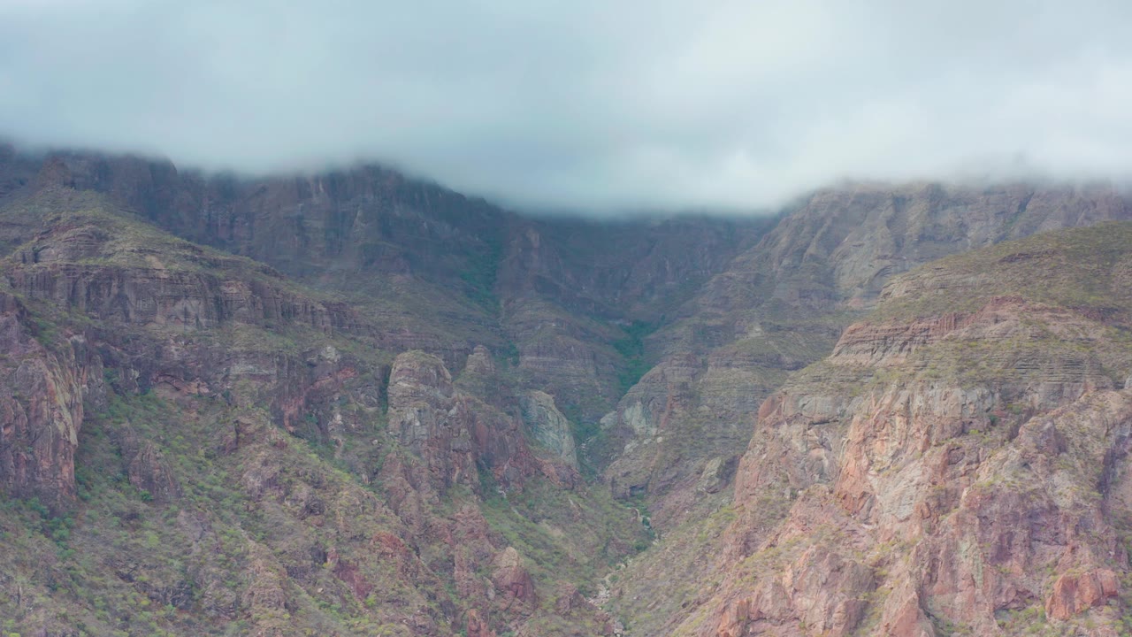 Puerto Escondido, Baja California Sur mountains with misty cloud cover softening the top of the cliffs, exposed brown rock faces, green ravine lines, and no visible people.