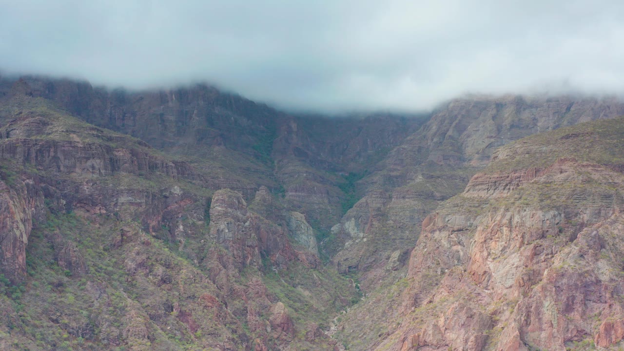 Opening frame of a rugged mountain valley in Puerto Escondido, Baja California Sur, with low clouds covering the upper ridges and no visible people.