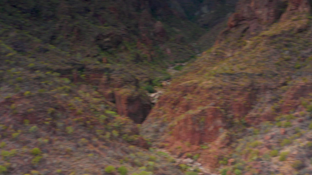 Rocky canyon wall with sparse green vegetation and a narrow valley channel.