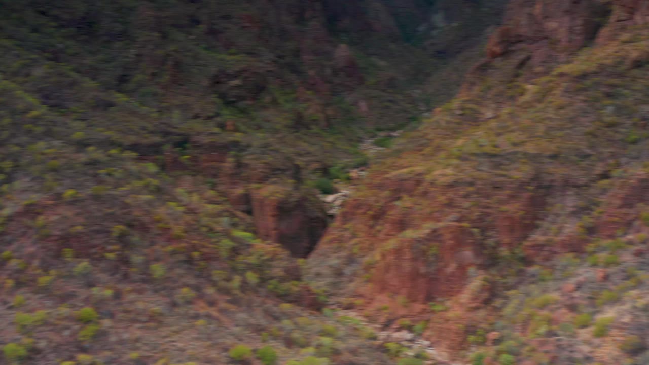 Puerto Escondido canyon valley with red rock faces, scattered shrubs, a small stream in the lower channel, and no visible people.