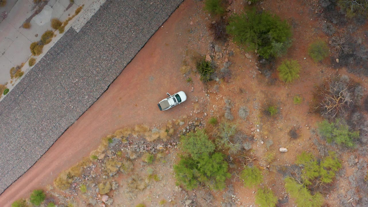 White car on a red dirt road beside gravel and desert shrubs.