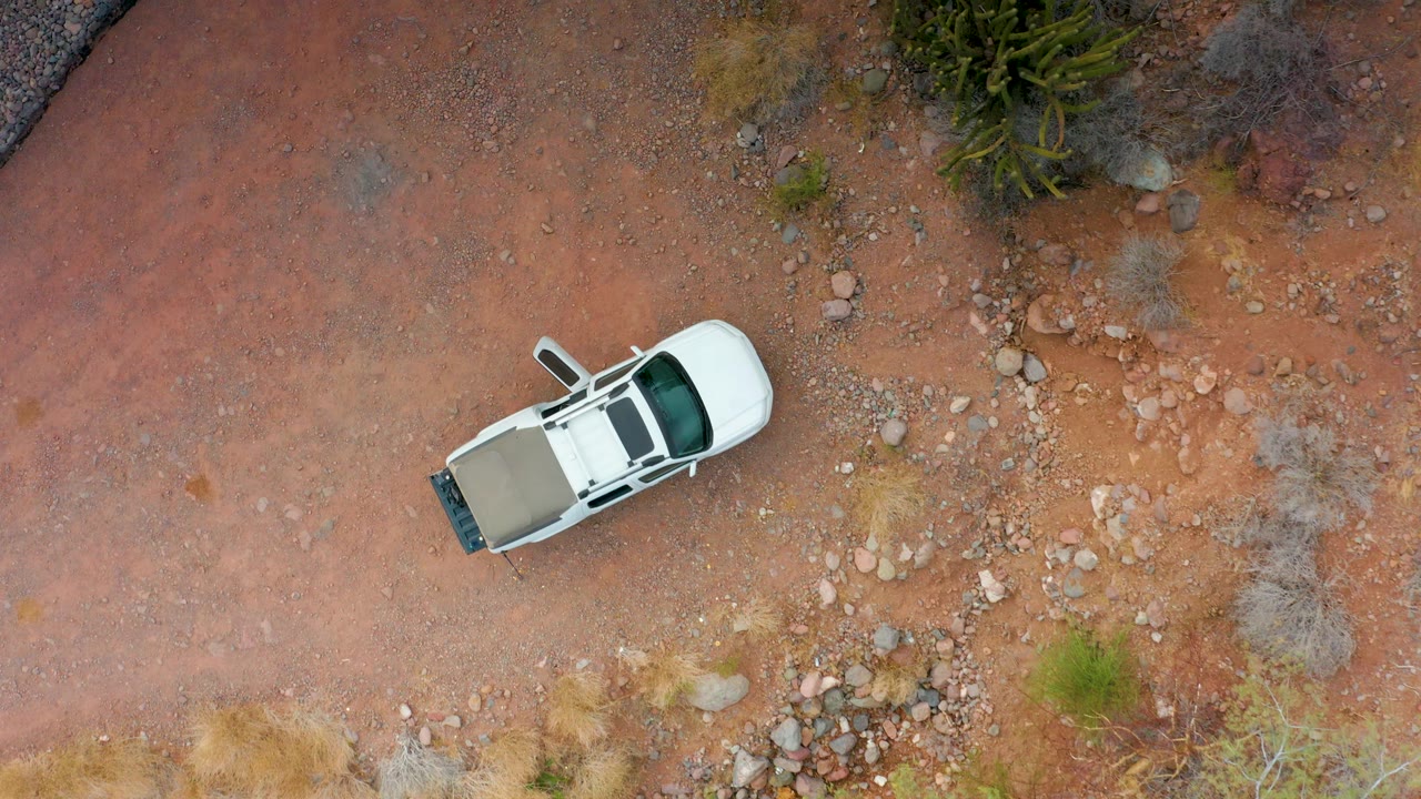 Overhead view of a white SUV on red dirt with rocks and shrubs.