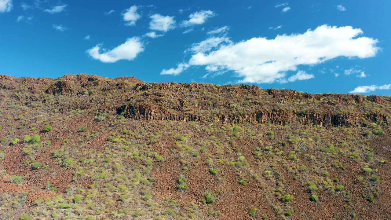 Dry rocky hillside and ridge beneath scattered white clouds.