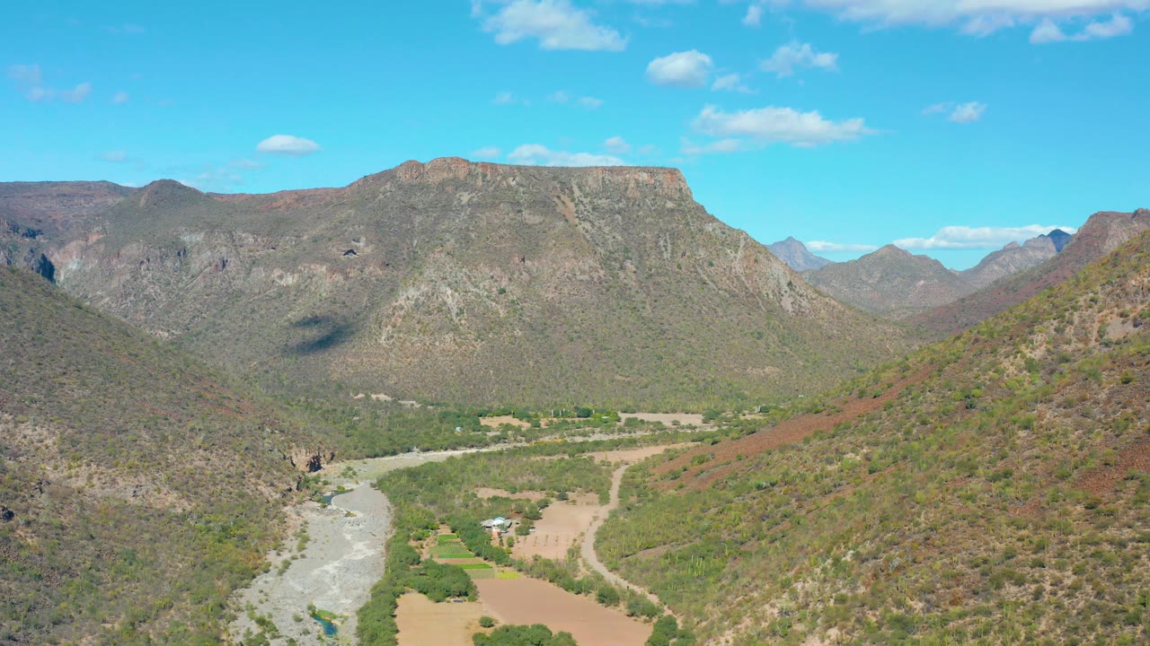 San Javier mountains fill the background while the river and sparse green vegetation run through the lower valley, with scattered clouds overhead and no visible people.