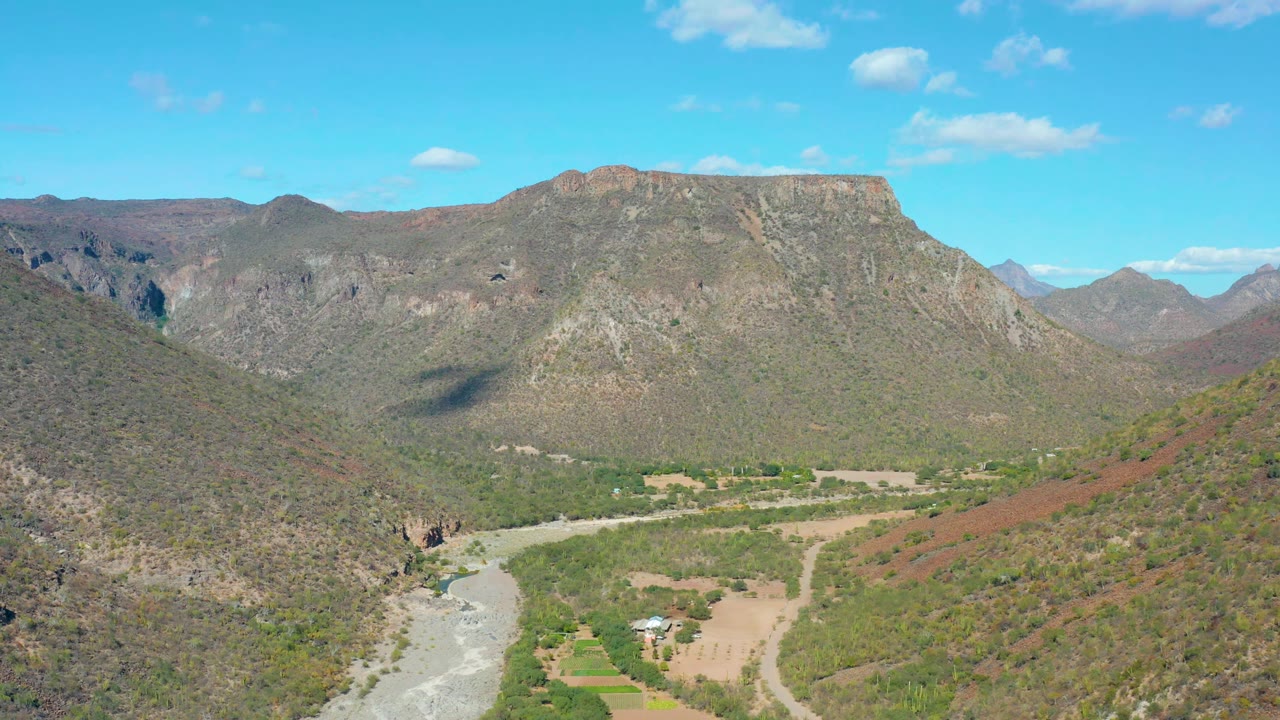 Wide aerial valley view with riverbed, fields, and surrounding mountains.