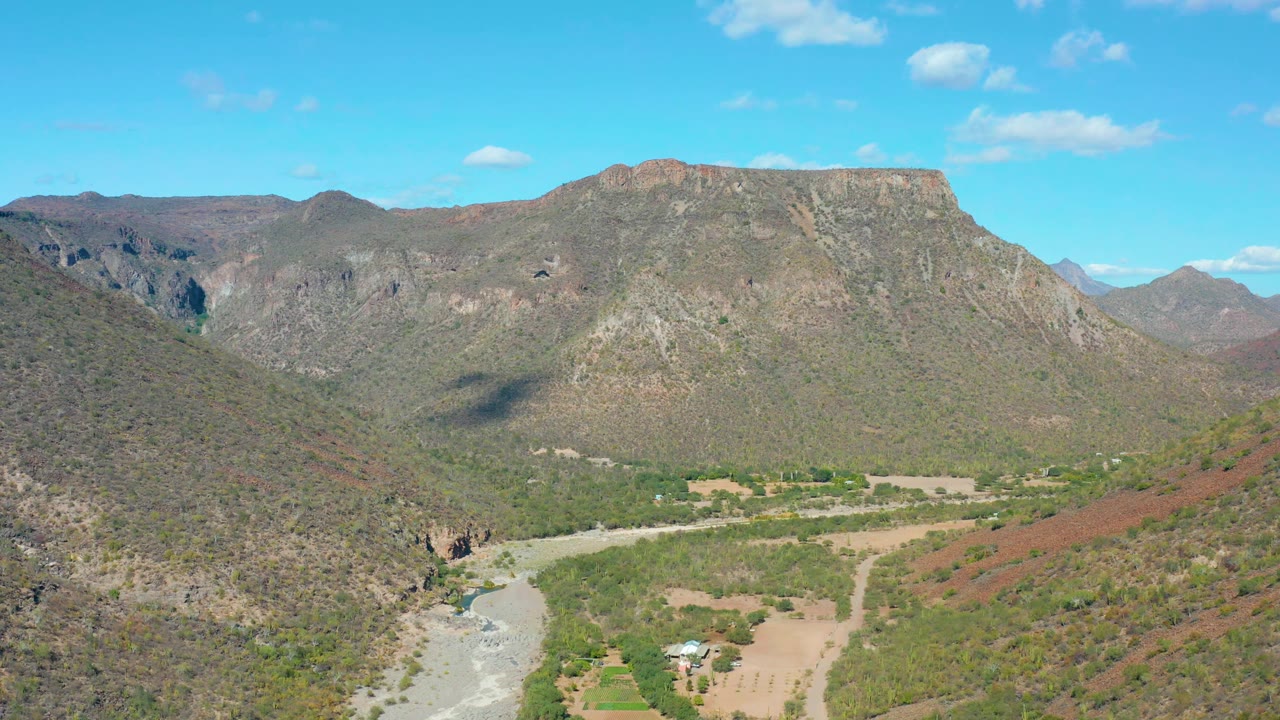 Aerial view in San Javier with the river channel curving through the lower left, dry rocky slopes rising on both sides, a flat ridge ahead, and no visible people.