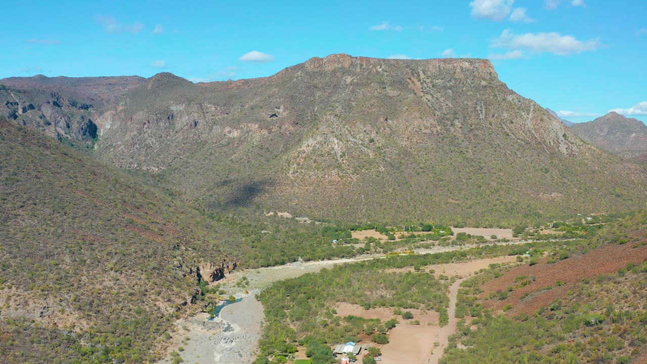San Javier aerial view holds on the broad valley, with a pale river wash in the lower left, green brush across the floor, and no visible people.
