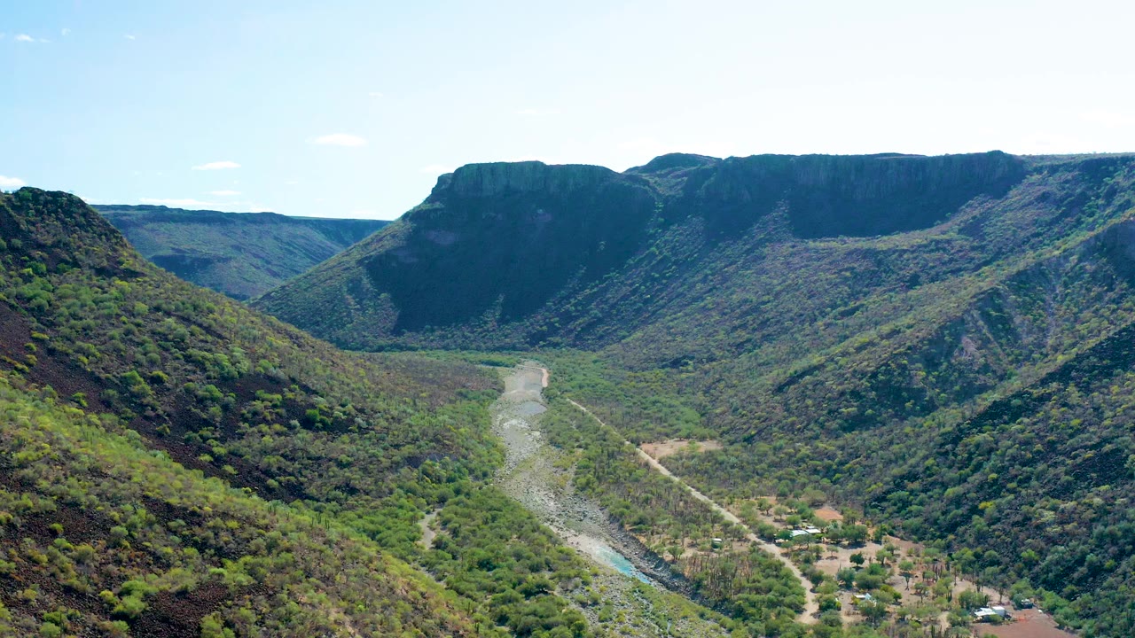 Opening frame of San Javier, Baja California Sur, showing a pale river winding through a green mountain valley beneath a bright sky, with no visible people.