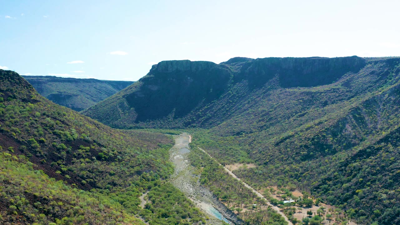 Wide aerial of a green valley with a river winding through mountain terrain.