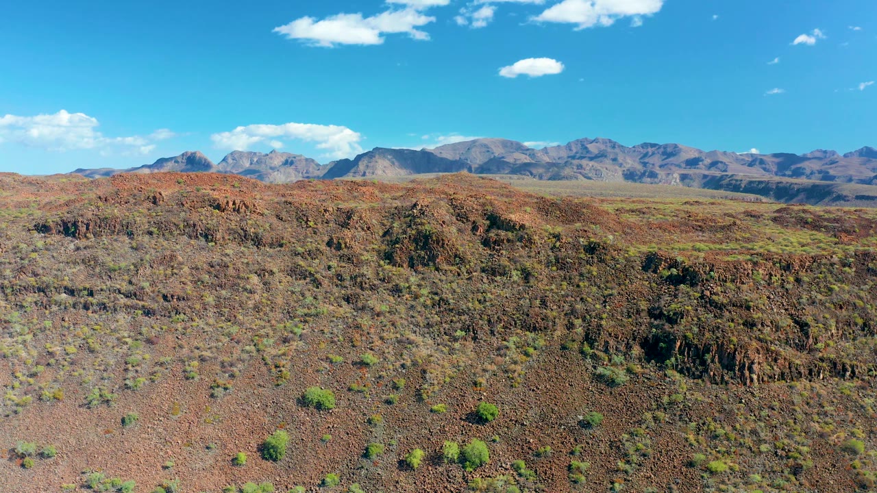 Early frame showing reddish-brown rock and scrub in San Javier, with the mountain range stretched across the background and no visible people.