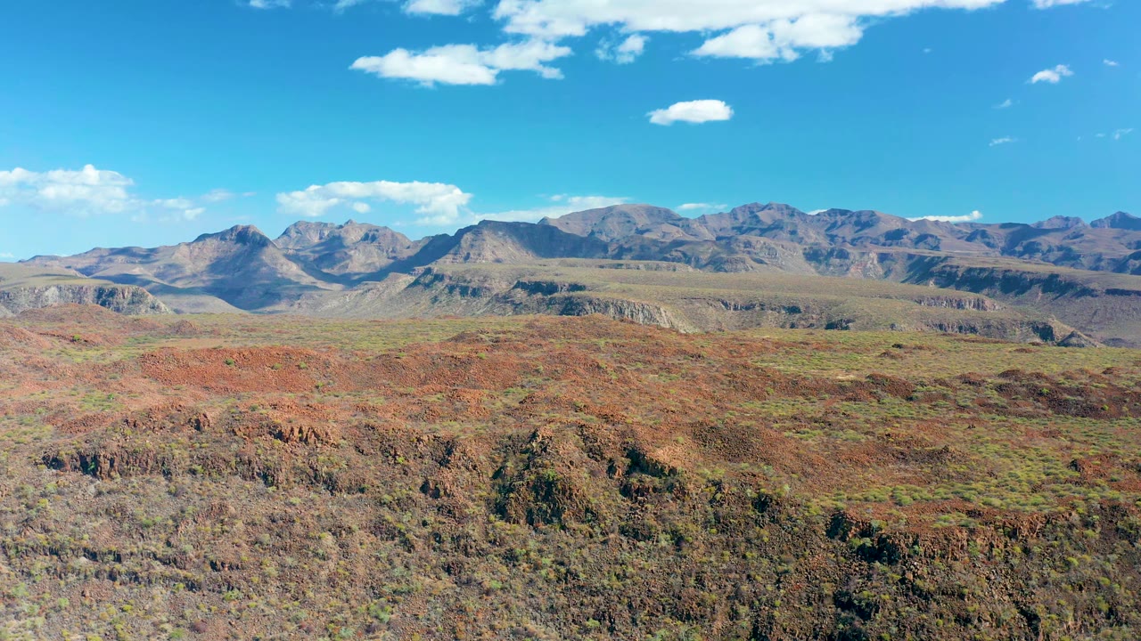 Desert rock formations and green patches below a mountain range.
