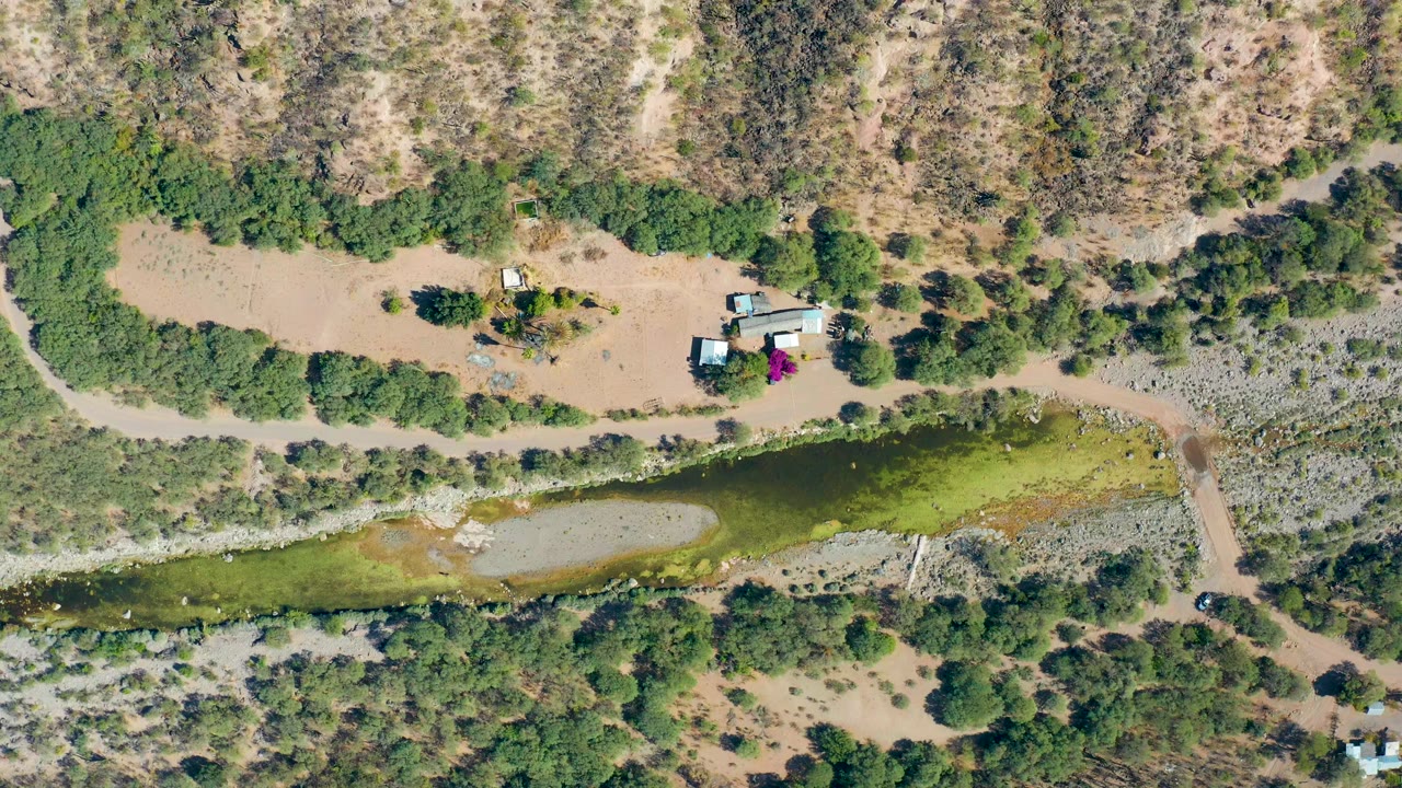 At 0:01, the San Javier aerial view holds on the pond and intersecting dirt paths, with dry hillsides, scattered trees, a small structure, and no visible people.